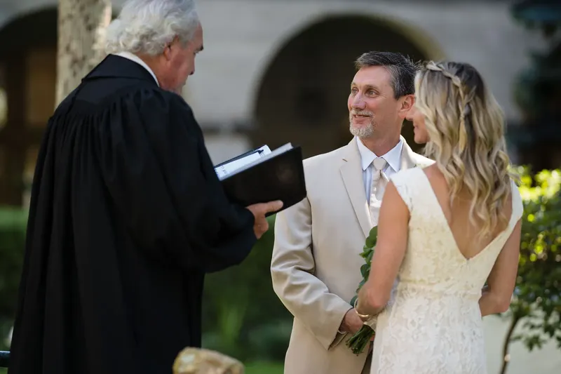 Groom smiling at bride during vows with officiant reading