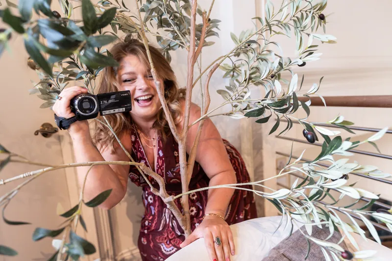 Bridesmaid laughing while filming with a camcorder through olive branches