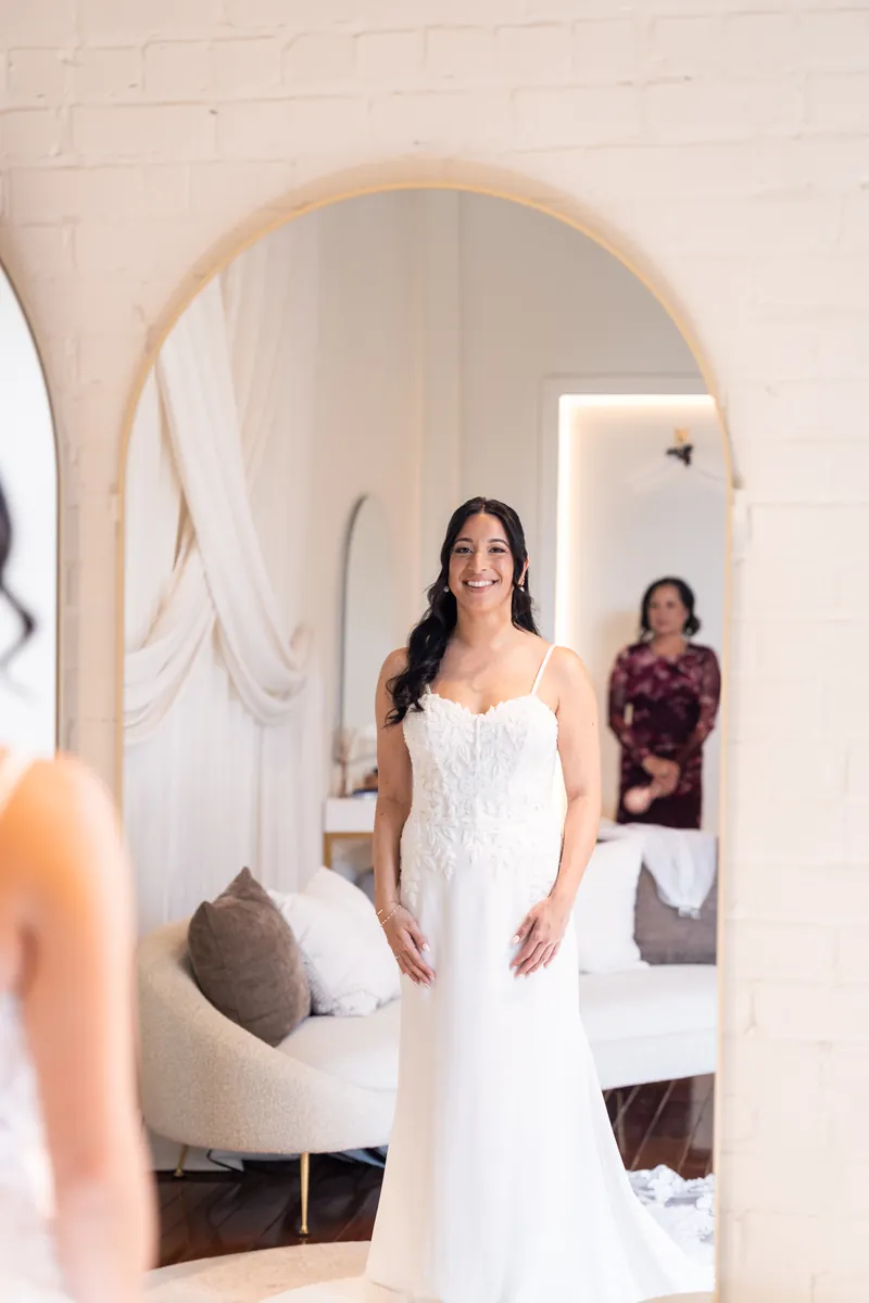 Bride smiling in her dress reflected in arched mirror in the Treasury bridal suite