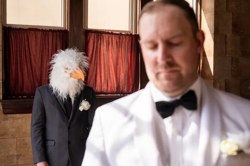 Groomsman wearing a chicken mask in a suit standing behind the groom before first look prank