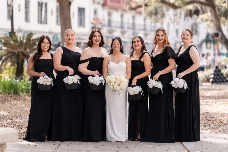 Bride and bridesmaids in black dresses holding white flower baskets on the plaza