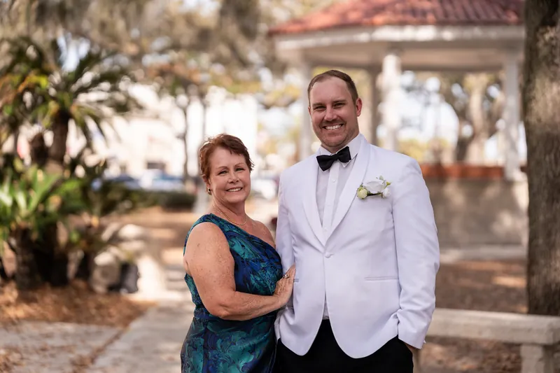 Groom and his mother posing together in the plaza under oak trees
