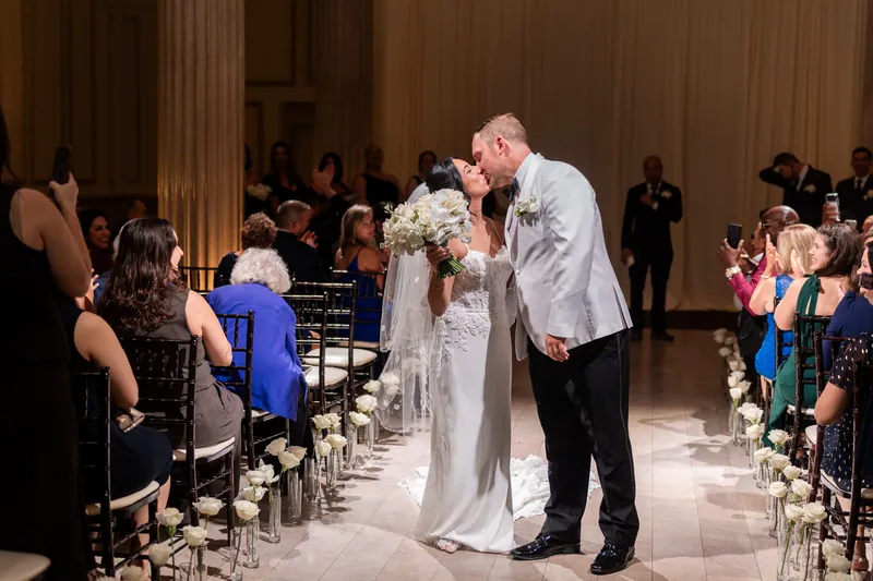 Bride and groom kissing while walking back up the aisle after ceremony as guests cheer