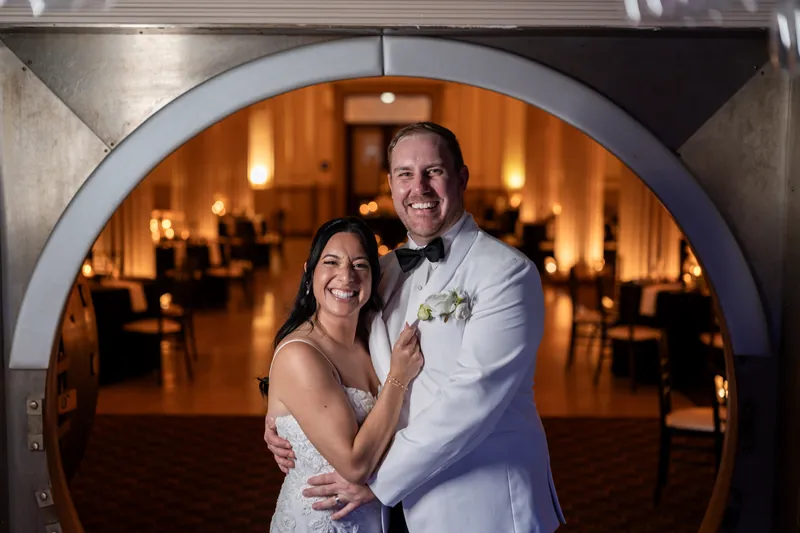 Couple laughing together framed inside the Treasury vault door with warm reception light behind them