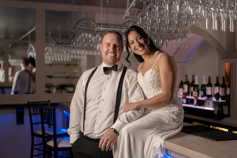 Bride and groom sitting together at the bar with wine glasses hanging overhead