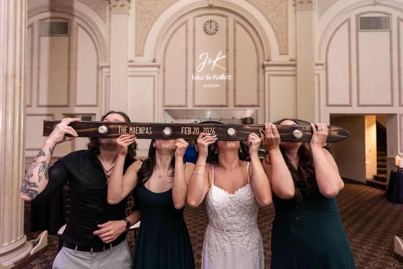 Wedding party doing shot ski with custom board reading The Maenpas Feb 20 2026
