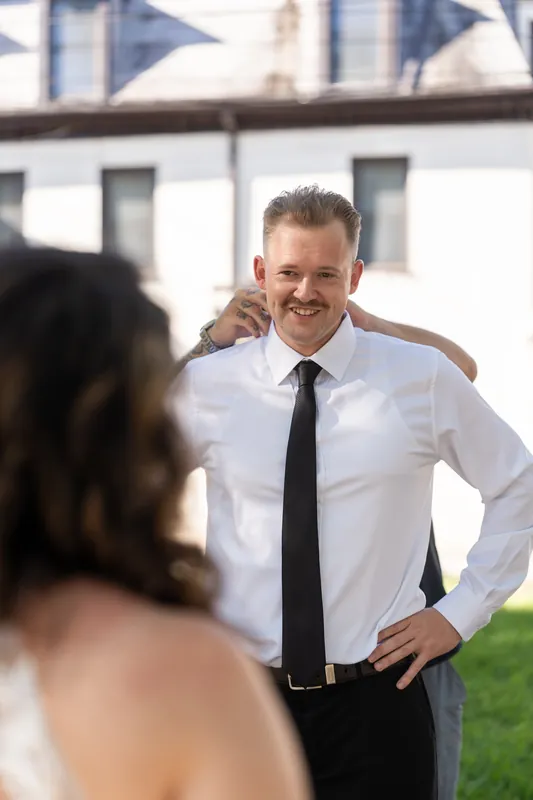 Someone in a white shirt and black tie smiles at their partner in a white gown, colonial buildings framing the scene behind them.