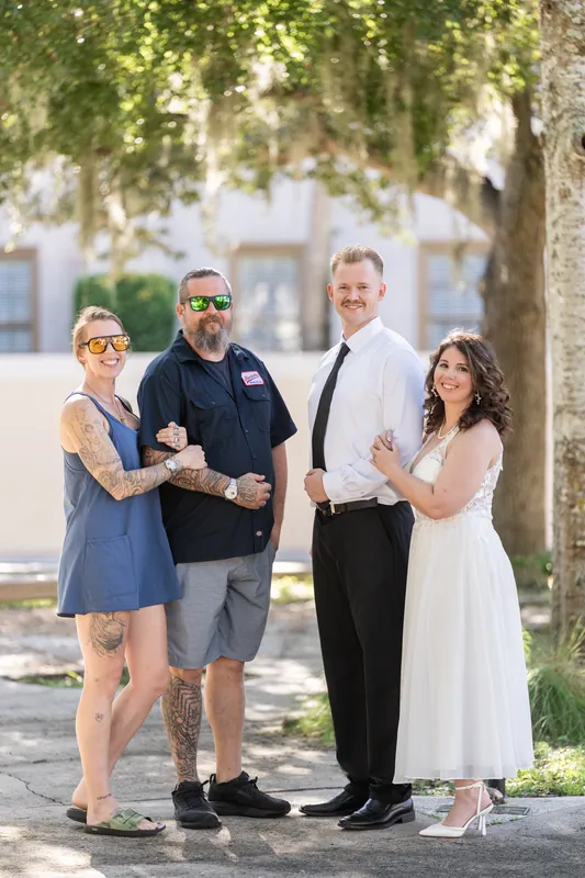 Two people with family members stand beneath a shaded tree in downtown St Augustine, dressed formally for an elopement celebration.