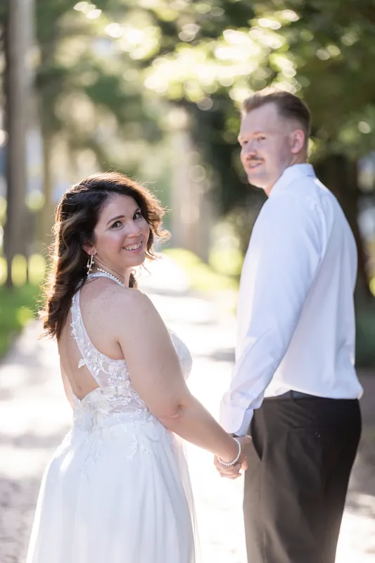 Kaley and Colton hold hands on a tree-lined street in Downtown St Augustine, with dappled sunlight filtering through the canopy behind them.