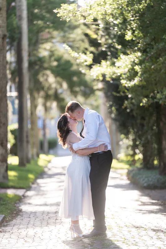 The couple shares a kiss under arching oak trees along a sunlit path in Downtown St Augustine.