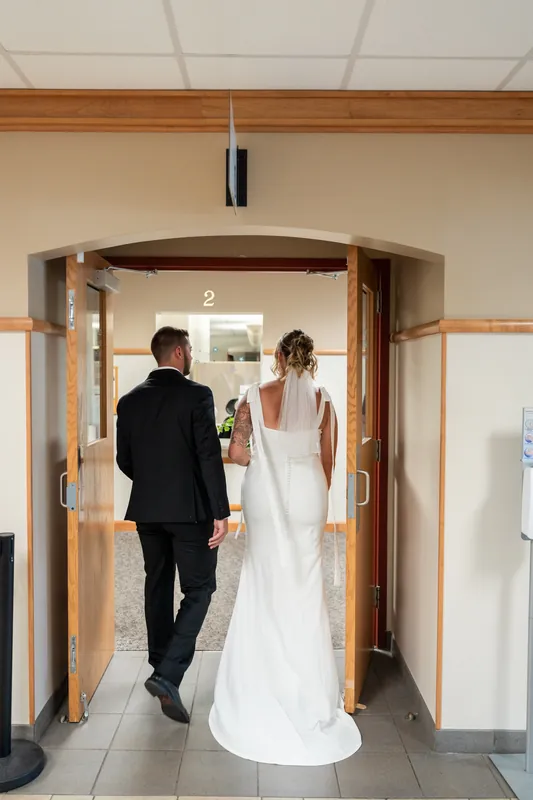 Matt and Kalsey walk together down a courthouse hallway, Kalsey's white dress trailing behind them.