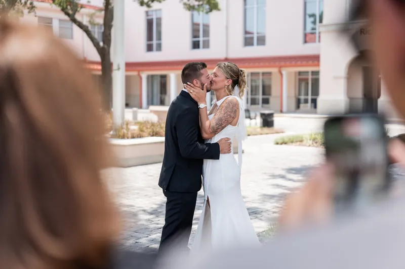 Matt and Kalsey kiss while courthouse guests watch from the foreground during their outdoor ceremony.
