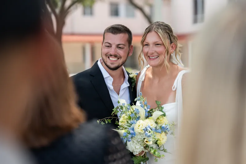 Kalsey holds her bouquet while smiling with Matt, framed by guests celebrating around them at the courthouse.