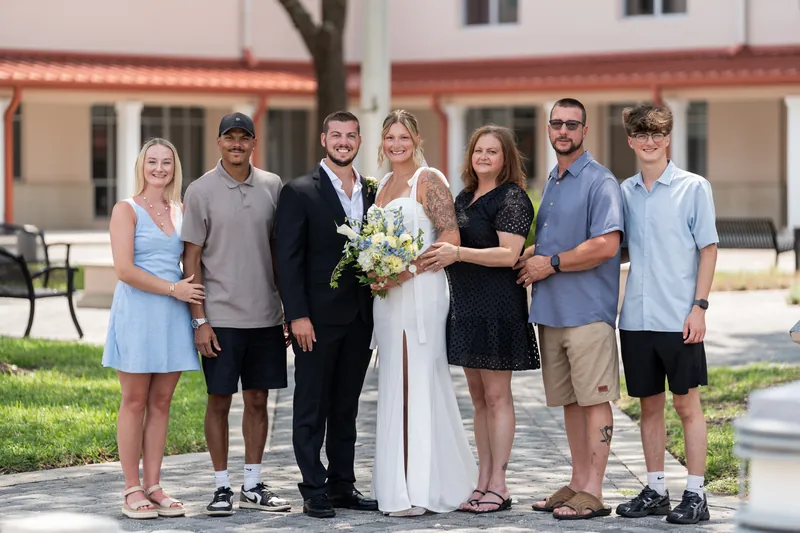 Kalsey and Matt stand with family members on the courthouse lawn, Kalsey holding a white and green bouquet.