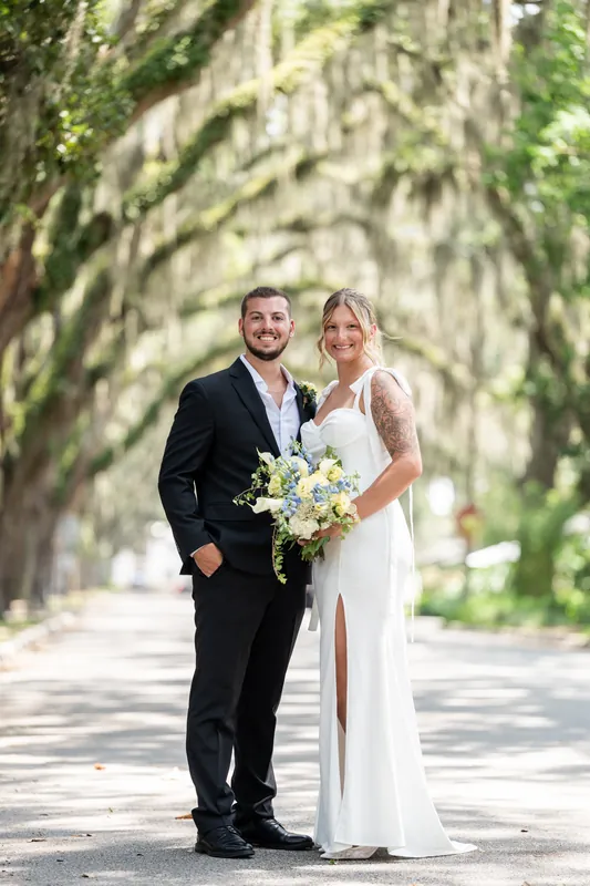Under a canopy of Spanish moss, Matt and Kalsey pose together holding their bouquet on a tree-lined street.