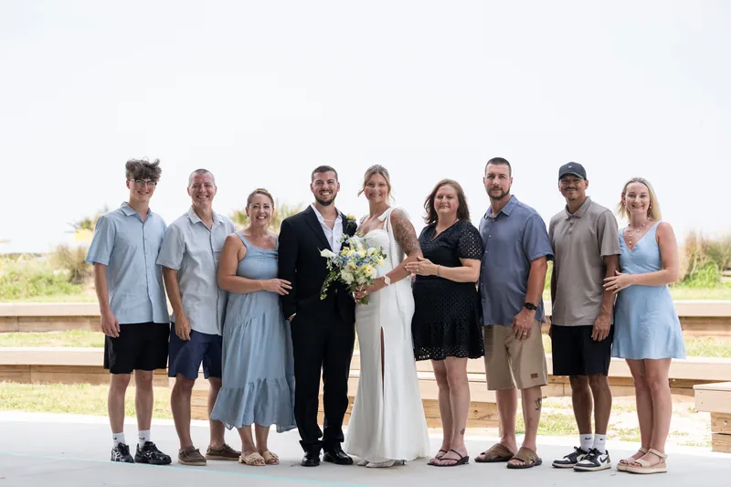 Kalsey and Matt stand together with ten family members on a boardwalk at Vilano Beach, all smiling at the camera under clear