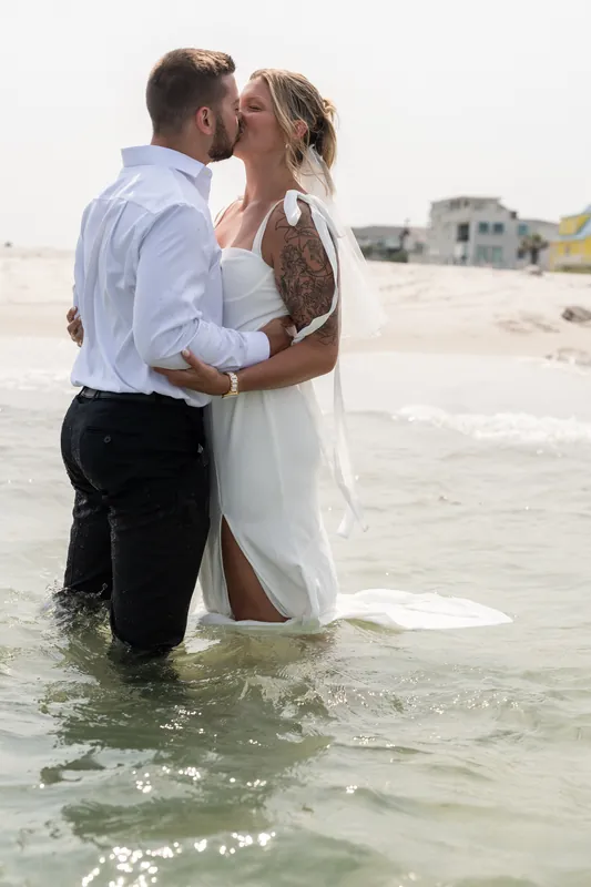 Matt and Kalsey kiss in knee-deep water while the sun glints off the waves around them at Vilano Beach.