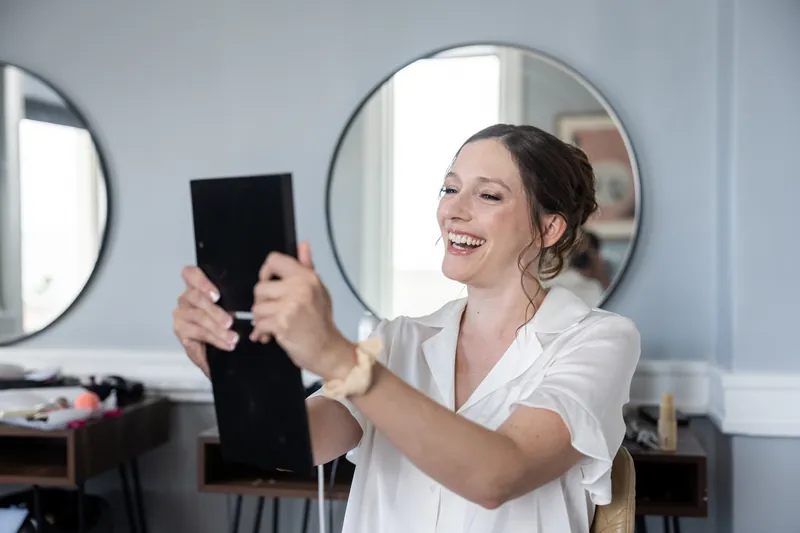 Katherine smiles while holding up a tablet in a brightly lit dressing room at The Treasury on the Plaza.