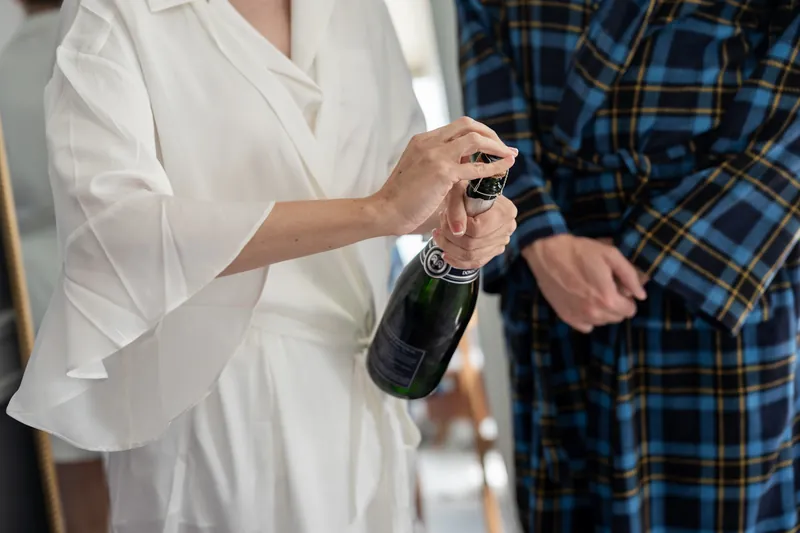 Katherine holds a champagne bottle while Nathan stands beside her in a blue plaid suit at The Treasury on the Plaza.