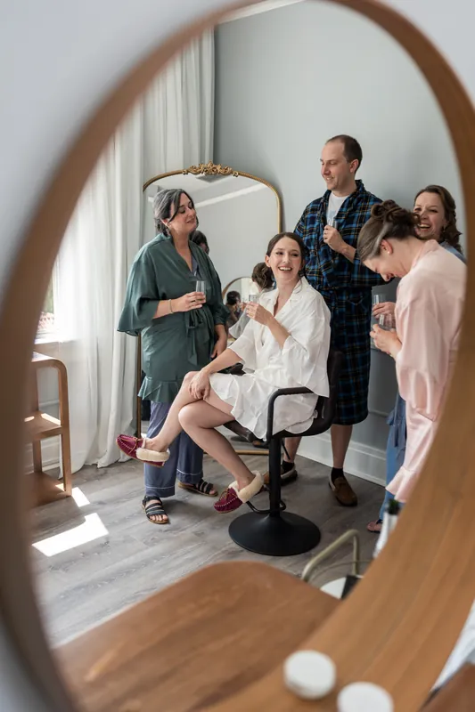 Guests gathered around Katherine, who sits in the center, are reflected in a large wooden-framed mirror during