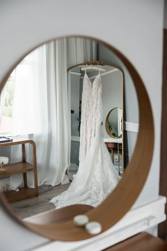 Katherine's lace wedding dress hangs from a rod, reflected in a round mirror at The Treasury on the Plaza.