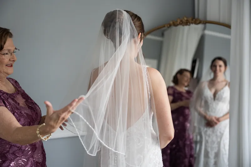 A woman in a burgundy dress adjusts Katherine's veil as she stands with her back to the camera at The Treasury on the Plaza.