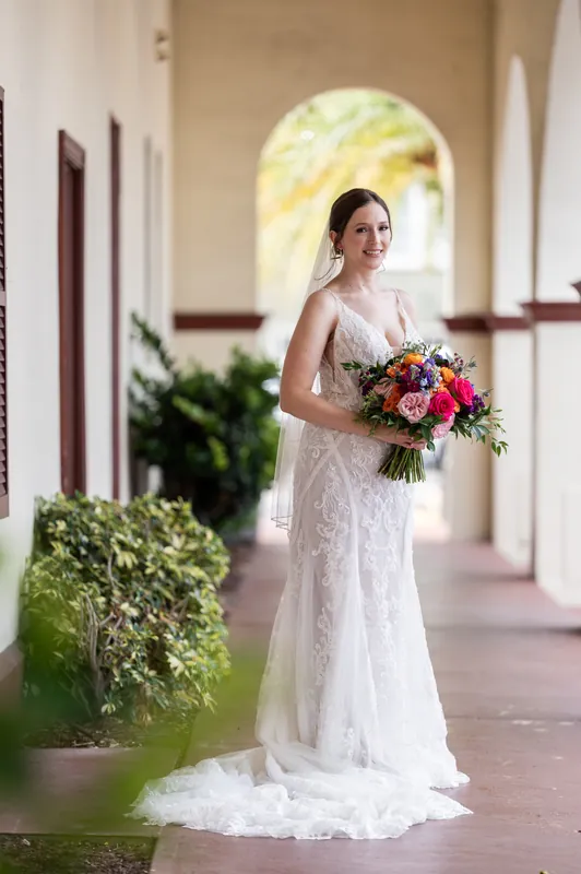 Katherine walks through the covered portico at The Treasury on the Plaza in her beaded lace gown, bouquet in hand.