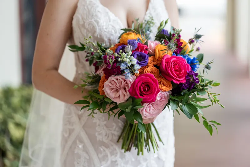Katherine's hands cradle a lush arrangement of roses, dahlias, and garden flowers in shades of coral, magenta, and purple.