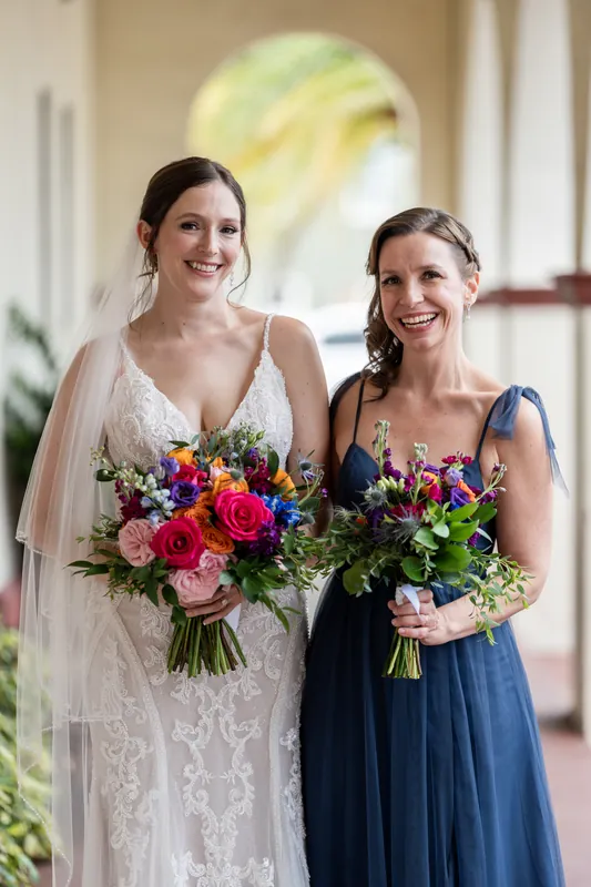 Katherine and a bridesmaid stand together under the arches at The Treasury on the Plaza, both holding coordinating bouquets.