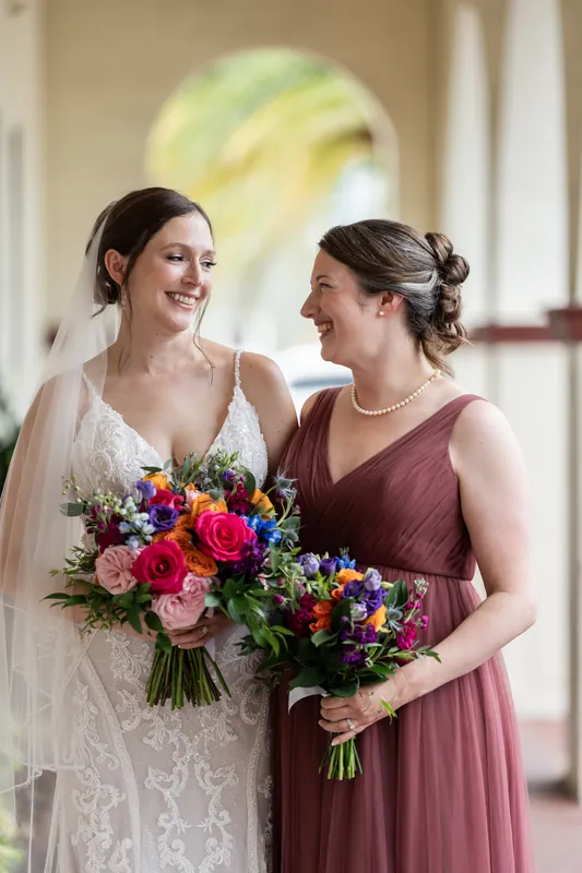 Katherine laughs with a bridesmaid in the colonnade at The Treasury on the Plaza, their bouquets held between them.