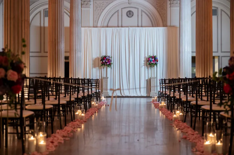 The ceremony aisle at The Treasury stretches between black chairs lined with pink rose petals and glowing candles, leading