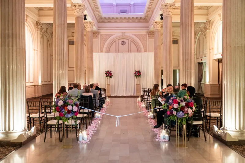 The ceremonial aisle at The Treasury on the Plaza stretches toward the altar, lined with ornate wooden chairs and lush floral