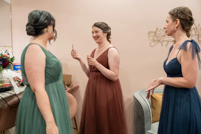Three guests in jewel-toned bridesmaid dresses converse near a table with flowers and wedding decor at The Treasury