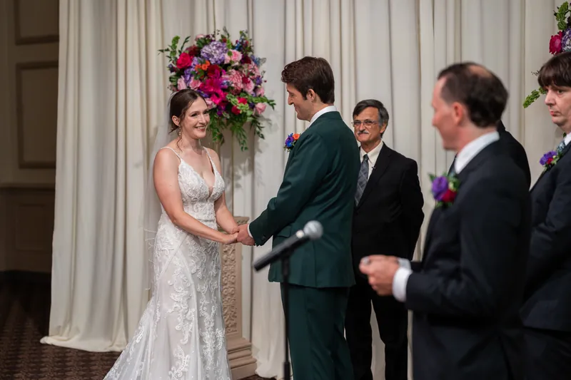 Katherine and Nathan hold hands and exchange vows in front of vibrant pink and magenta floral installations.