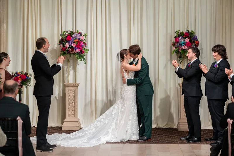 Nathan embraces Katherine after their first kiss, her train trailing behind them as wedding party members applaud.
