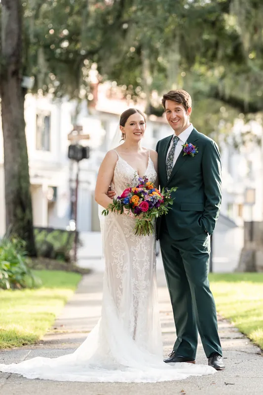 Katherine and Nathan stand beneath draped trees on the plaza, Katherine holding a jewel-toned bouquet in an ivory lace gown