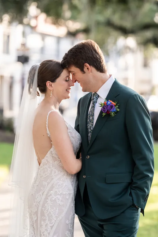 Katherine and Nathan face each other closely, foreheads nearly touching, both smiling as they stand on the lawn.