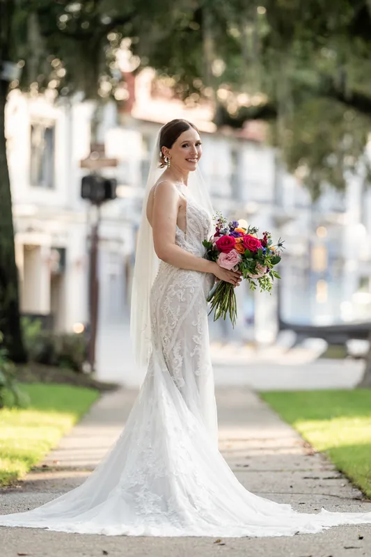 Katherine poses alone on the plaza in her beaded ivory gown, holding her vibrant bouquet and looking over her shoulder.