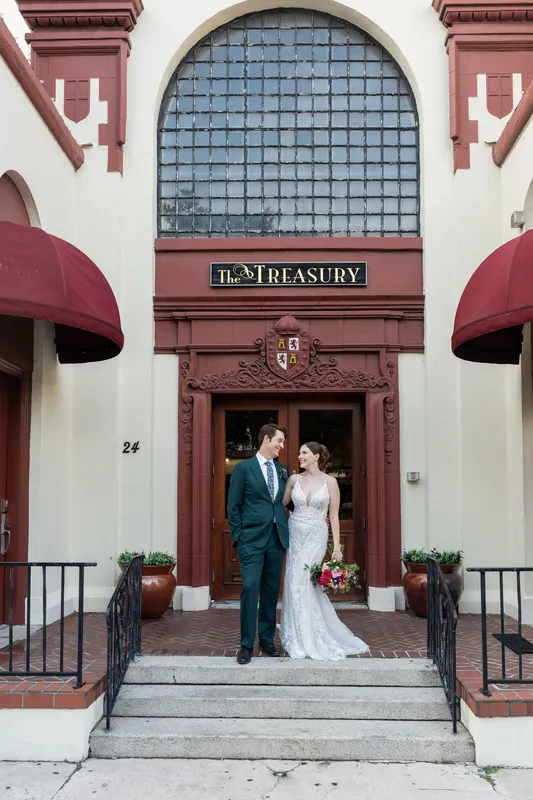 The couple stands centered in the doorway of The Treasury's iconic arched entrance, framed by burgundy awnings and ornamental