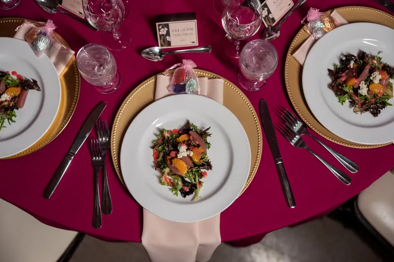 Overhead view of a round table set with burgundy linens, gold-rimmed plates, and colorful plated salads at The Treasury