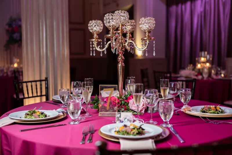 Illuminated candelabra with hanging crystals anchors a magenta-linened table beneath purple drapes at The Treasury