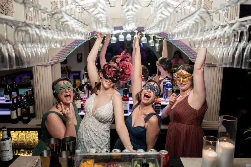 Four women in the ornate barrel-vaulted room raise their arms in celebration as Katherine lifts her bouquet overhead