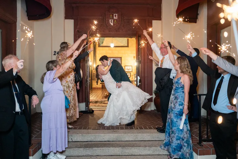 Katherine and Nathan walk beneath a sparkler-lined archway of raised arms from their guests outside The Treasury
