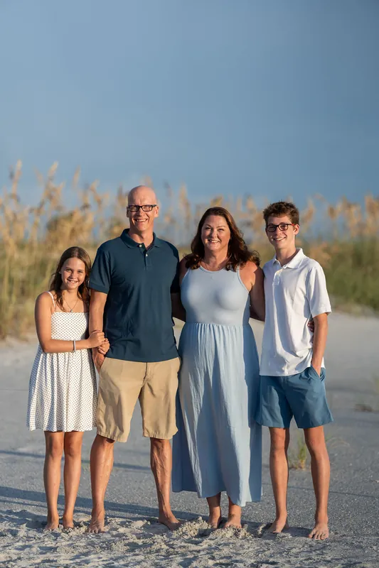 Four people spanning different ages stand together on the beach at Vilano Beach, with sea oats and dunes in the background.