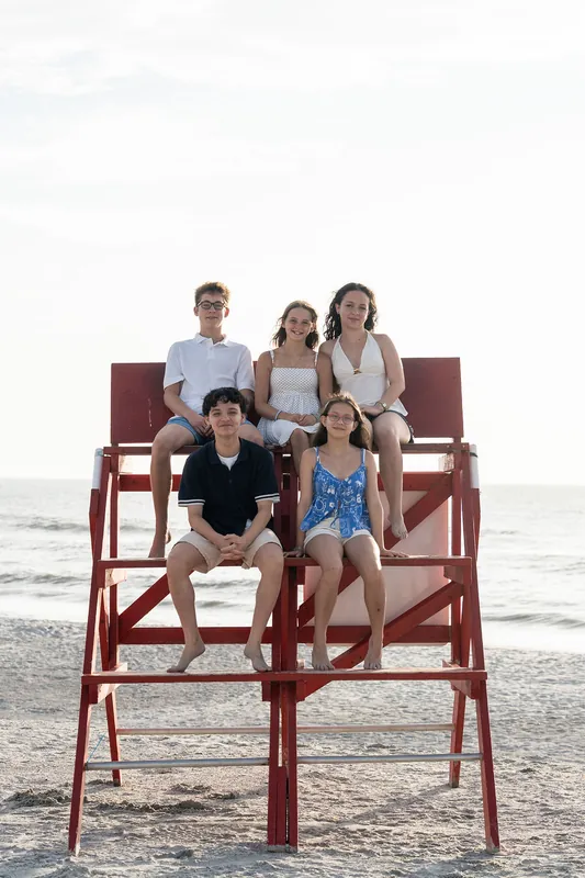 Five family members pose together on a large red wooden lifeguard chair at Vilano Beach, with the ocean and overcast sky