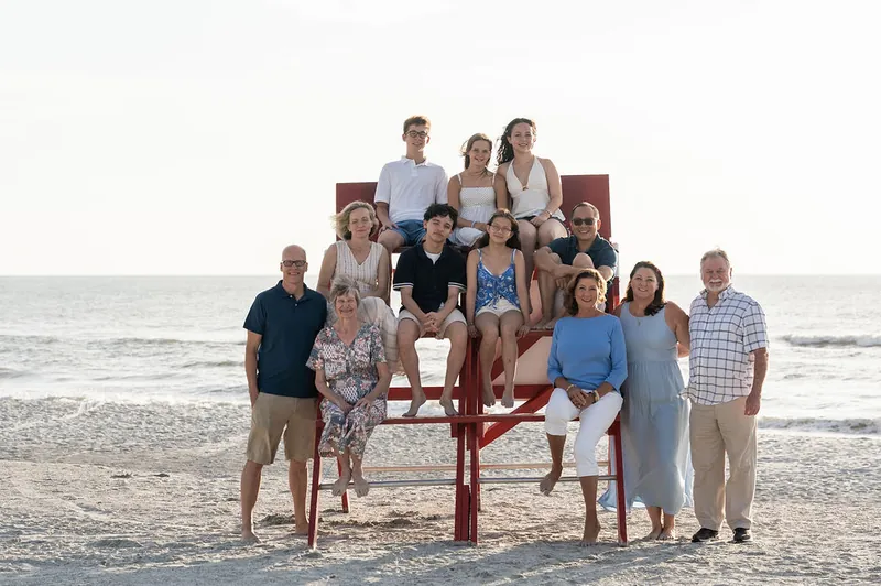 Eleven family members stand and sit on red wooden lifeguard chairs at Vilano Beach, arranged in rows with the shoreline