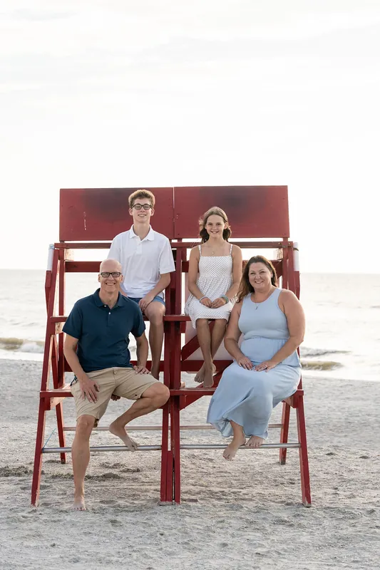 Four adults sit and stand on red wooden lifeguard chairs at Vilano Beach, with calm ocean water stretching behind them.