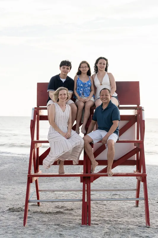 Six family members arranged on red wooden lifeguard chairs at Vilano Beach display casual summer clothing against the grey