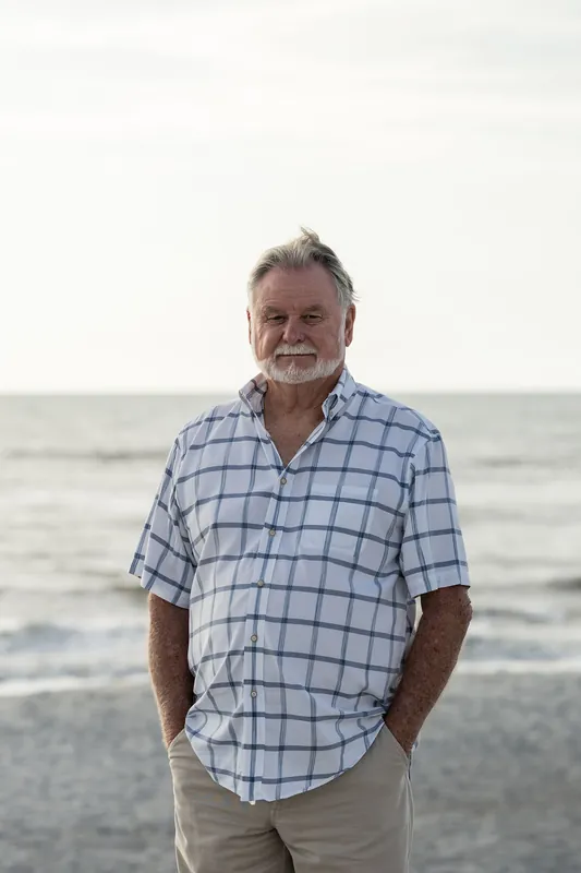 A man in a blue plaid shirt stands alone on the sand at Vilano Beach with the ocean horizon behind him.