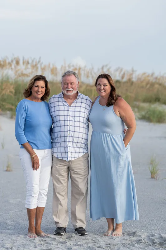 Three adults stand together on the sand near beach dunes at Vilano Beach, with the ocean and sea oats visible